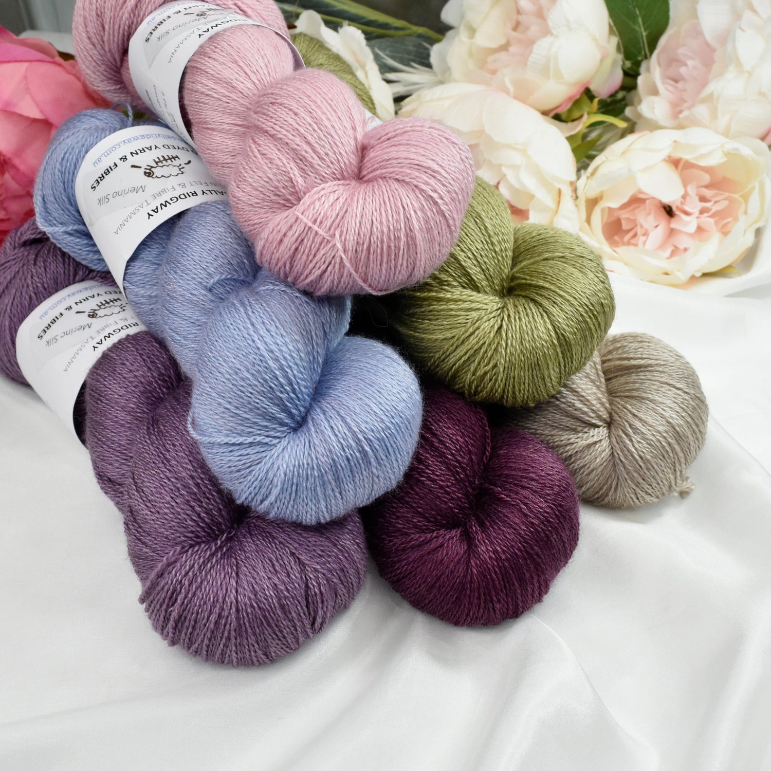 a stack of 6 hand dyed lace weight knitting yarns by sally ridgway with flowers int he background
