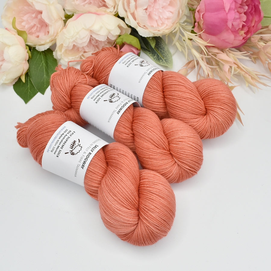 3 skeins of hand dyed 4ply knitting yarn in soft apricot laying side by side pointing down. Shop hand dyed yarn online