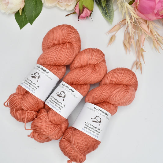 3 hanks of hand dyed 4ply knitting yarn in soft apricot laying side by side on a 45 degree angle. Shop hand dyed yarn online
