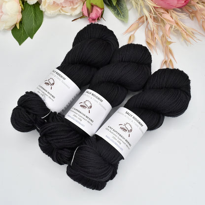 3 skeins of black hand dyed dk 8ply knitting yarn facing the top on a 45 angle with flowers in the background Buy knitting yarn online now