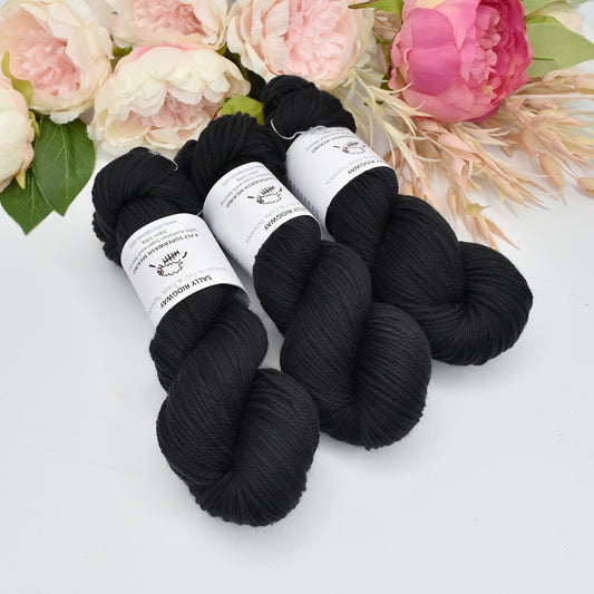 3 skeins of black hand dyed dk 8ply knitting yarn facing the bottom with flowers in the background Buy knitting yarn online now