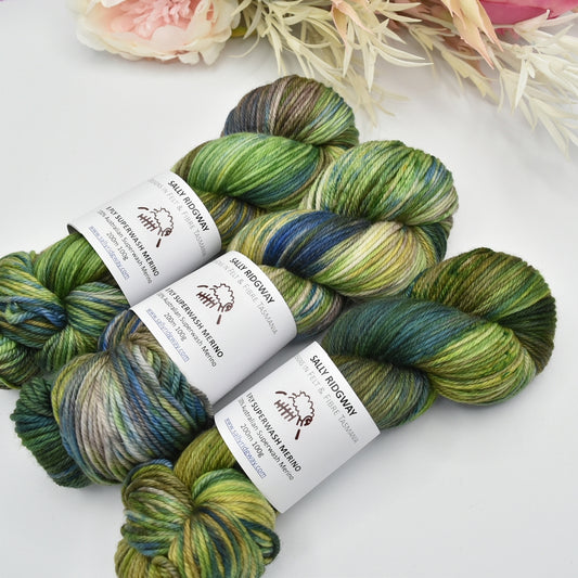3 hanks of hand dyed sock knitting yarn on an angle with flowers. Buy online now