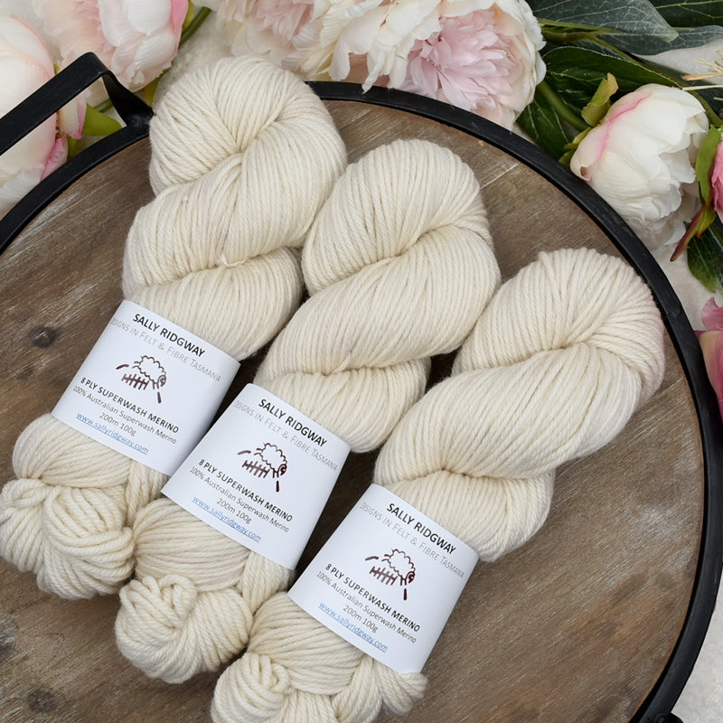 cream hand dyed 8 ply knitting yarn laying on an angle on a wooden tray. Shop hand dyed yarn online